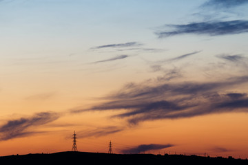 The sun sets behind the horizon and illuminates power lines