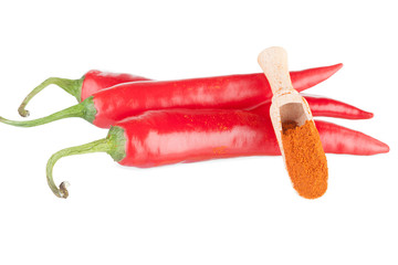 Three pods of chili and ground paprika in a wooden spoon