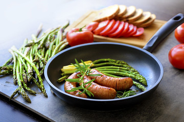 Fried sausages with asparagus, tomatoes and rosemary on a pan
