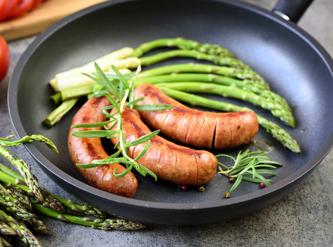 Fried sausages with asparagus, tomatoes and rosemary on a pan