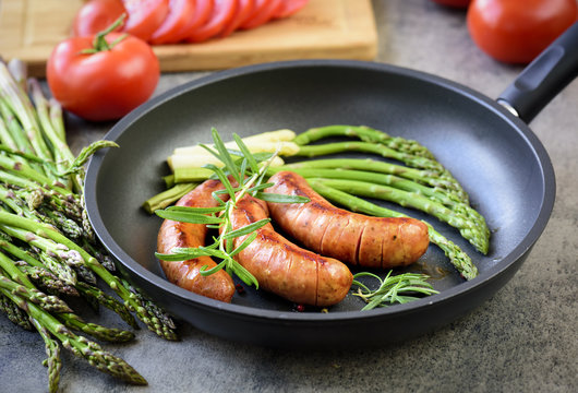 Fried sausages with asparagus, tomatoes and rosemary on a pan
