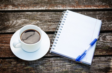 Coffee cup, notepad  and pen on wooden background