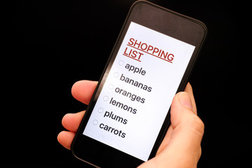 Shopping List on smart phone display in woman hand. Black background.