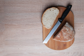 Cutting board, bread and a knife lying on a wooden table