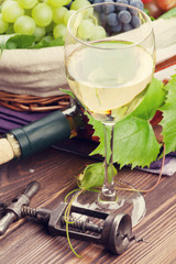 White wine glass, bottle and grapes on wooden table