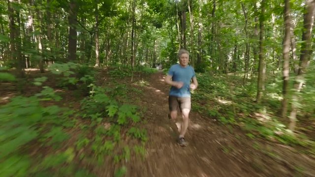 Adult man running jogging outdoors in a forest nature on a forest trail and enjoying it and looking happy