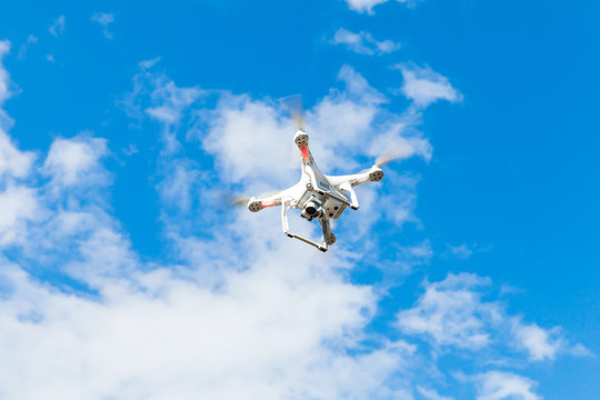 White quadrocopter flying in blue cloudy sky, drone