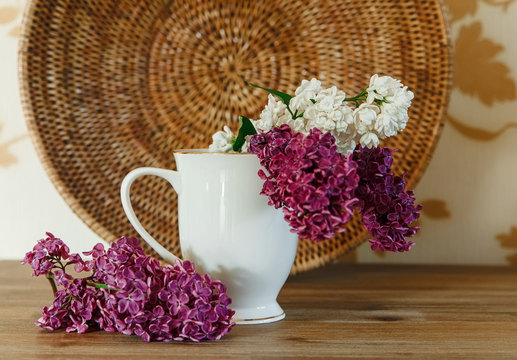 Two Branch of White and Purple Lilac in the Ceramic Cup.Rattan Plate.Wooden Background,Selective Focus