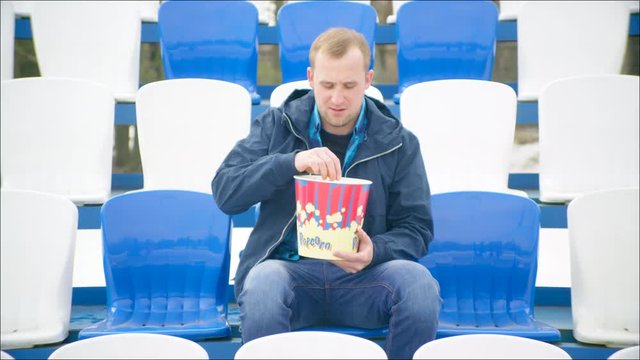A guy sat on the tribune with popcorn bucket