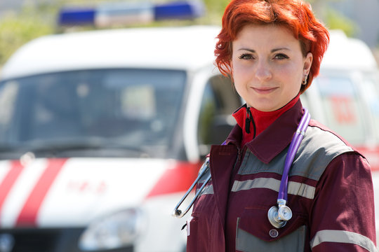 Positive female paramedic standing at ambulance machines background