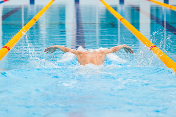 dynamic and fit swimmer in cap breathing performing the butterfly stroke