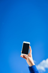 Closeup on hand taking sky photo with smart phone, blue background