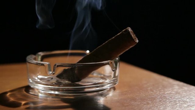 Burning cigar in ashtray.Smoking cigar in an ashtray on dark background