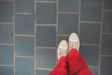 Female legs in sneakers on the background paving slabs.