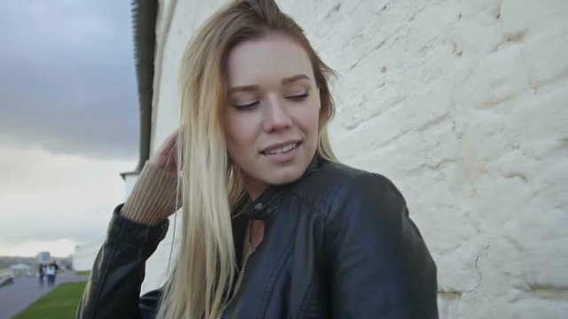 girl with long blonde hair in leather jacket posing in the city straightens hair slo-mo