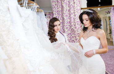 Naklejka premium Female trying on wedding dress in a shop with women assistant.