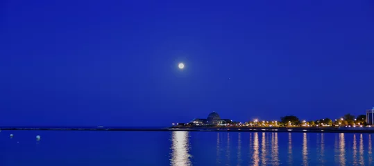 Fototapeten Blue Moon Over calm Waters reflecting lights © BradleyWarren