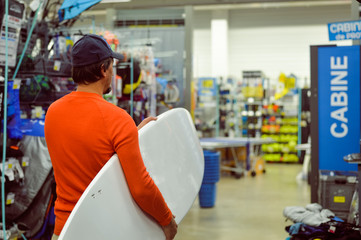 Back view of man holding a white surf board on shop background indoors