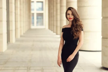 Poster Young elegant girl posing at city street. Pretty beautiful business woman in elegant black dress against city background. © Dmitry Tsvetkov