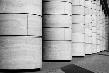 Row of marble columns with dark gaps and pavement floor. Black and white photo. Architectural details with rhythm