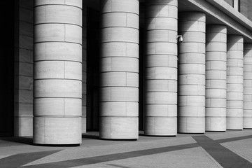 Row of marble columns with dark gaps and pavement floor. Black and white photo. Architectural details with rhythm