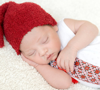 sleeping newborn baby in ukrainian embroidery and red hat with hand on head