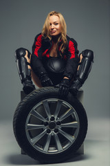 Fototapeta na wymiar Female in motorcycle uniform posing with car wheel.