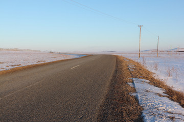 The asphalt rural road going among snow fields
