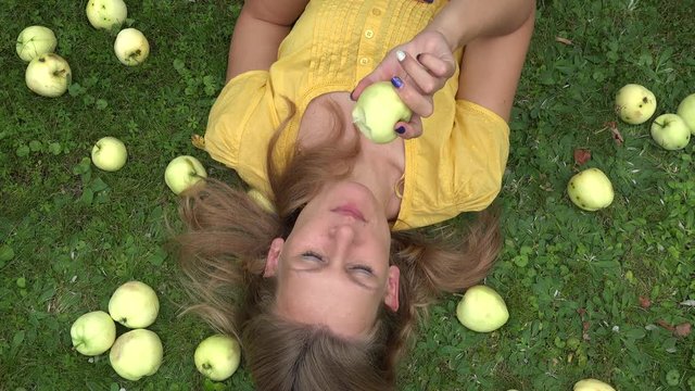Beautiful smiling young woman lying on grass and bit taste apple fruit. 4K