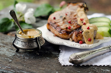 Pork steak, mustard in a jar on the table. Vintage style.
