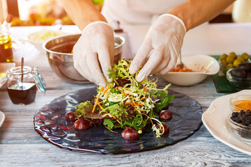 Hands touch salad on plate. Hands of cook in gloves. This dish is almost ready. Salad with grape and arugula.