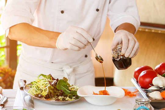 Hands Holding Jar And Spoon. Sauce Pouring Onto Raw Fish. Juicy Salad And Red Fish. Chef Knows The Best Recipe.