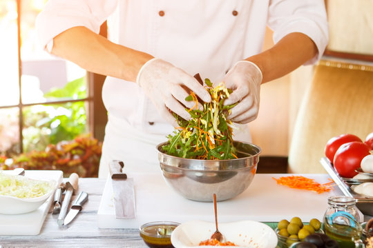 Man's hands make salad. Salad bowl on cooking board. Shredded carrot and fresh arugula. Chef prepares healthy meal.