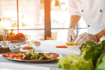 Hands with knife cut pepper. Cook in gloves prepares food. Chef's workplace beside window. This work requires inspiration.
