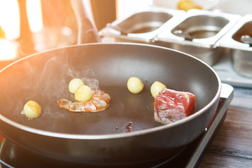 Shrimp on frying pan. Raw fish piece and potatoes. Thermal processing of food. Electric cooker in bistro kitchen.