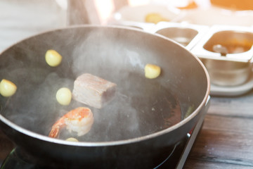 Potatoes and shrimp on pan. Steam coming from frying pan. Food ingredients for special dish. Fried prawn and tuna.