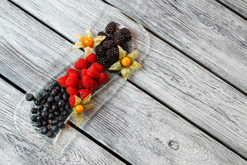 Naklejka premium Blueberry and raspberry on plate. Berry dessert on wooden background. Fresh sweet berries. Add vitamins to your diet.