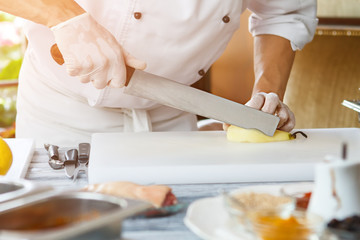 Hand with knife cuts pear. Pear on white cooking board. Cafe chef prepares fruit. Fresh ingredients only.