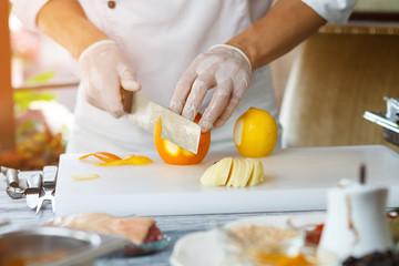 Obraz na płótnie Canvas Hand with knife peels orange. Orange on cooking board. Chef needs some orange rind. Ingredient for meat dish.