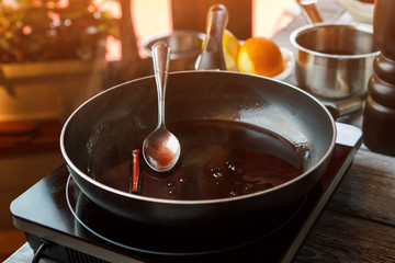 Pan with liquid and spoon. Cinnamon stick and dark liquid. Wine sauce with cinnamon. Sweet aroma...