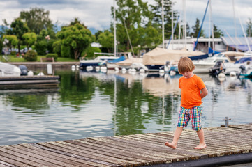 Fototapeta premium Cute little boy playing by the lake at sunset, wearing bright orange tee shirt and colorful shorts