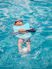 Asian boy swimming with the board in the pool