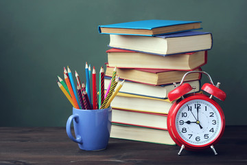 A stack of books, pencils and alarm clock on the table.