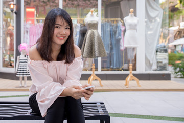 Charming young woman in white shirt reads or texts message to mobile phone, against old grunge houses in old city.