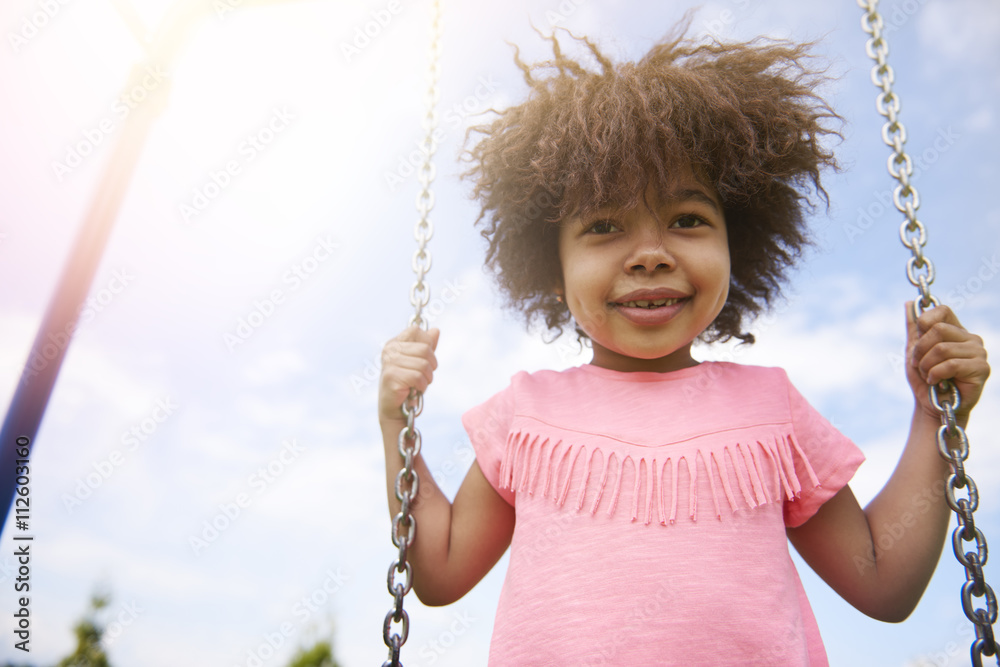 Wall mural Cute little girl swinging in sunny day