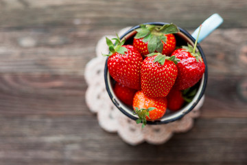 Fresh juicy strawberries in old rusty mug. Rustic wooden background with hand made crochet napkin. Top view, place for text.