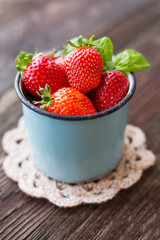 Fresh juicy strawberries  in old rusty mug. Rustic wooden background with crochet napkin.