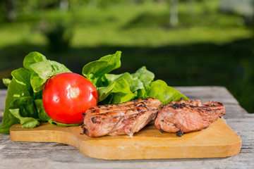 Two grilled chicken Breasts and red tomato with lettuce on wooden cutting Board on old wooden table on green background