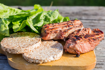 Two chicken Breasts on the grill and red tomato, with a salad and two diet-bread on a wooden cutting Board on old wooden table on green background