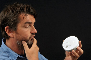 Homme regardant un détecteur de fumée avec un air circonspect 